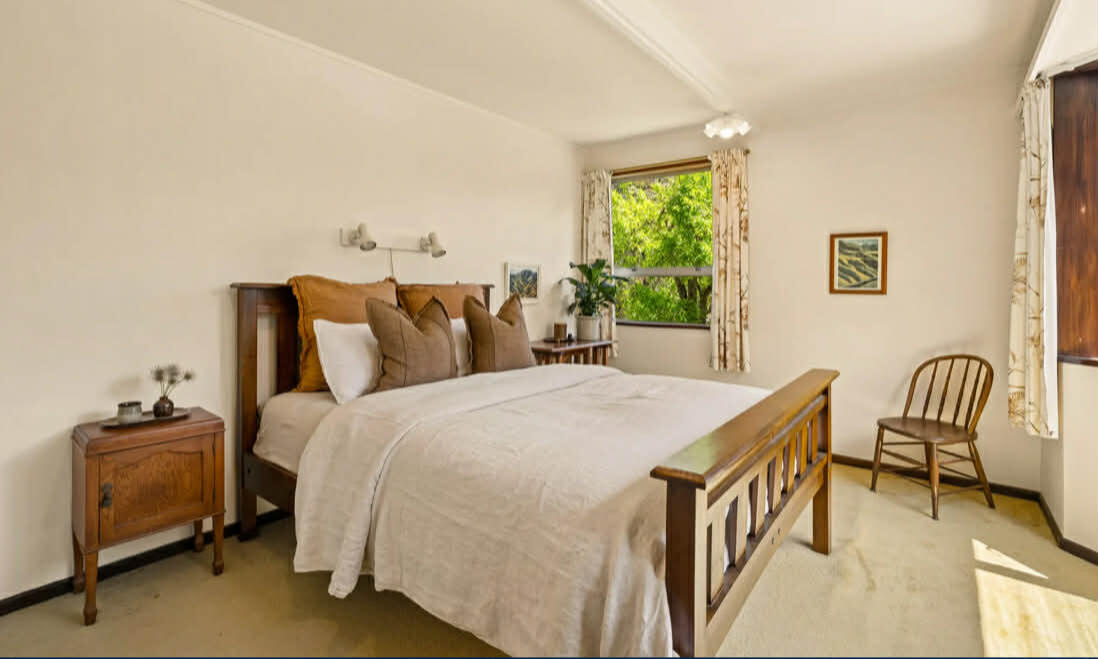 Airy bedroom with white bedding, wooden furniture, and green garden views through the window
