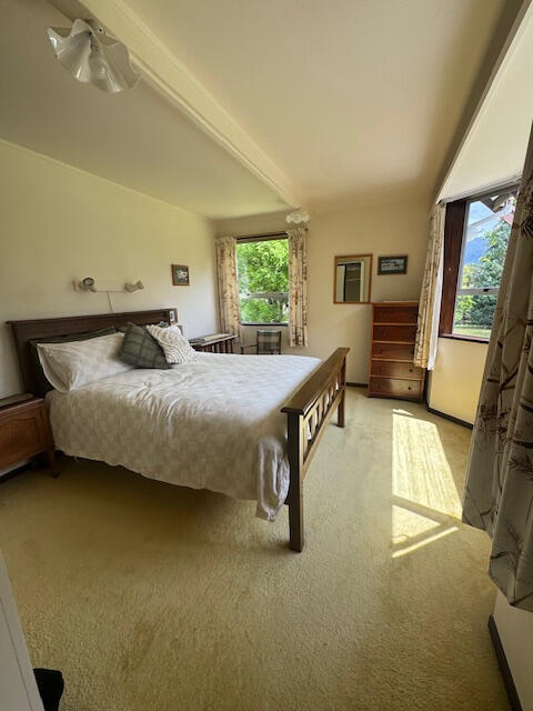 Bright bedroom with a double bed, white walls, wooden floor, and a garden-view window