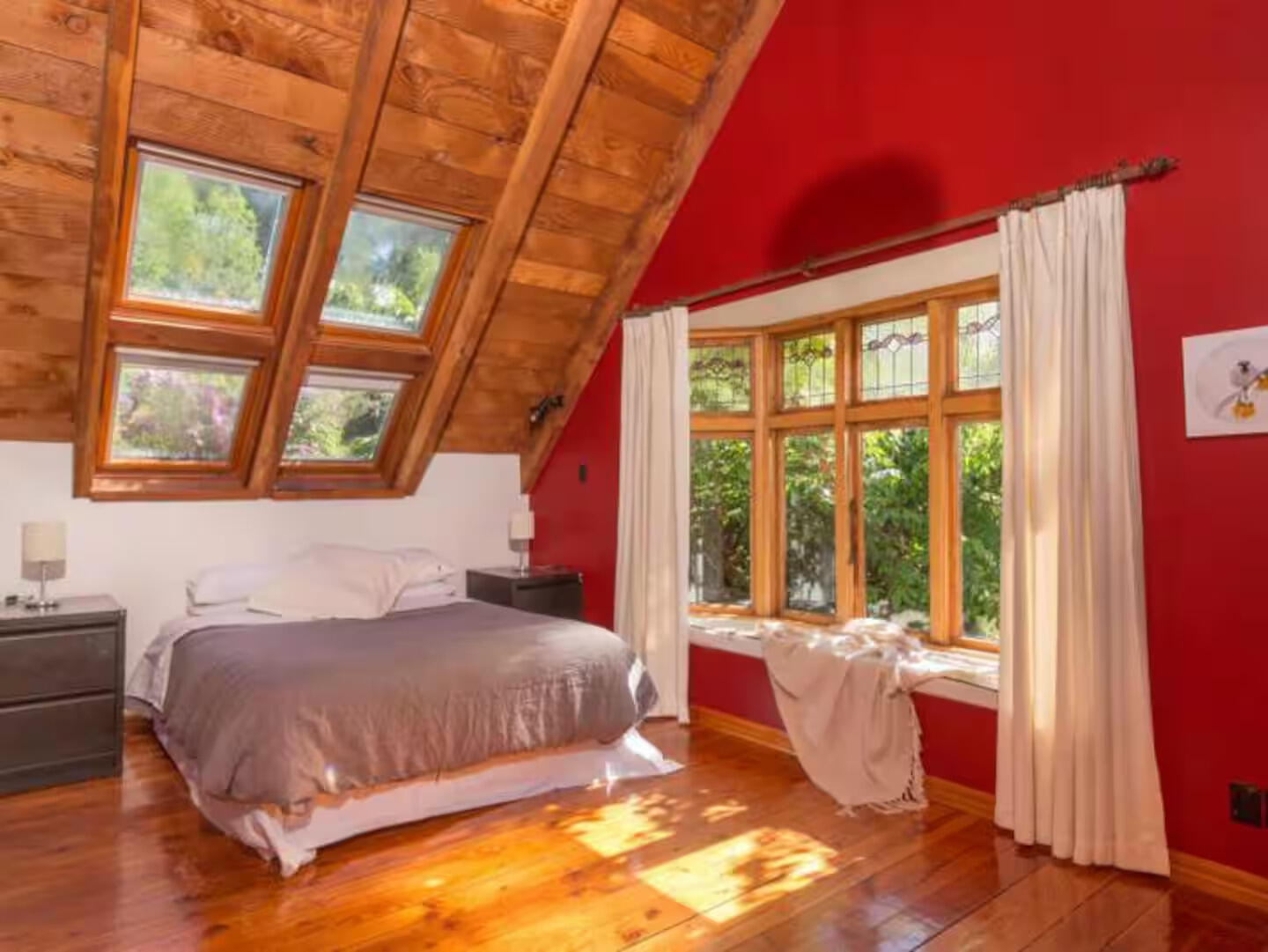 Attic bedroom with skylights, red walls, and a single bed with natural light flooding in