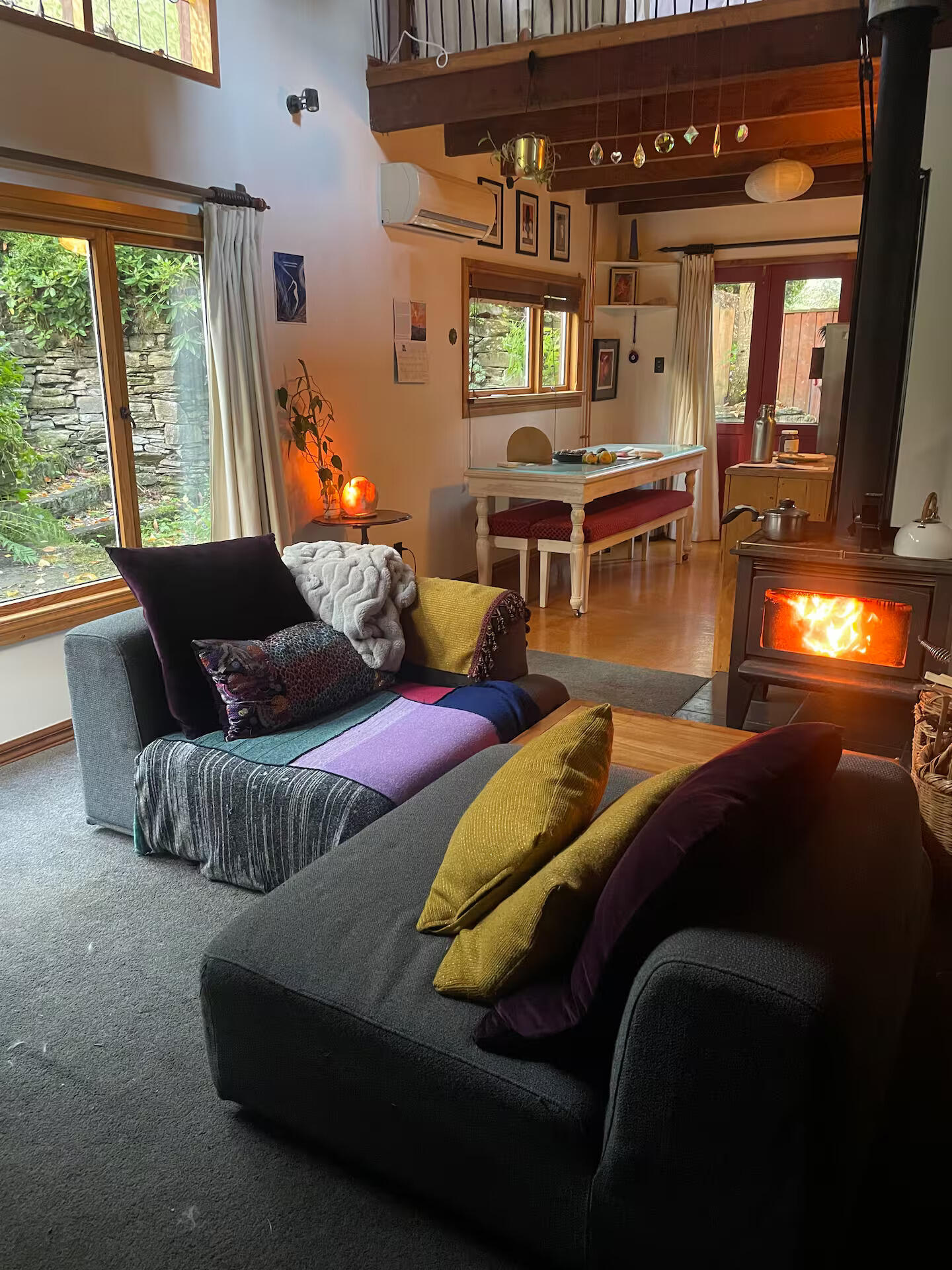 Cozy living room with a lit fireplace, colourful cushions on a sofa, and warm wooden flooring