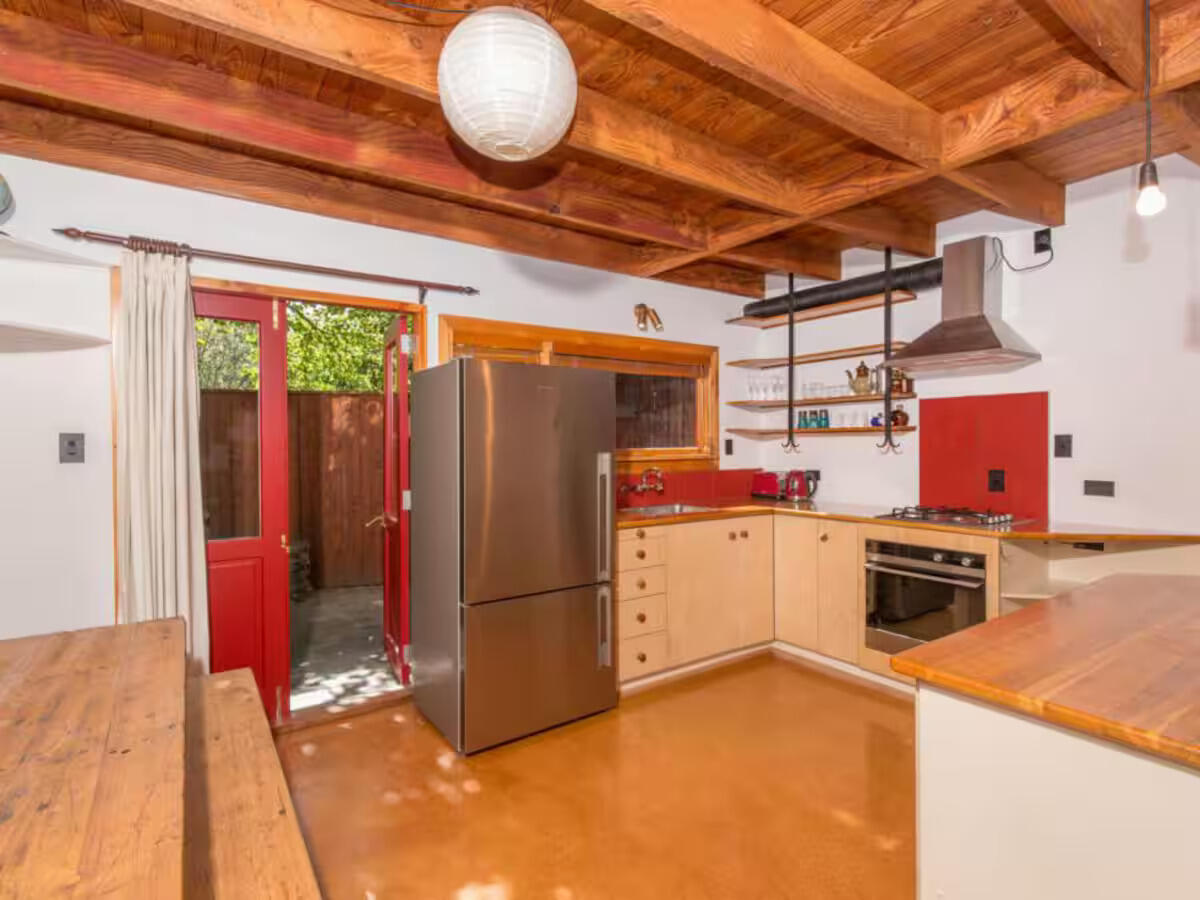 Rustic kitchen with exposed wooden beam ceiling, stainless steel fridge, red accents, and hardwood floors